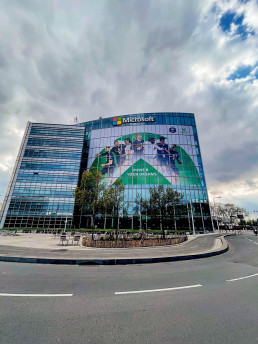 Façade du bâtiment Microsoft habillée d'une immense bâche publicitaire de la campagne 'Power Your Dreams'.